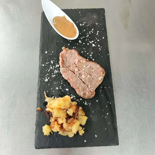 Un filete y patatas en un plato negro con una cucharada de salsa