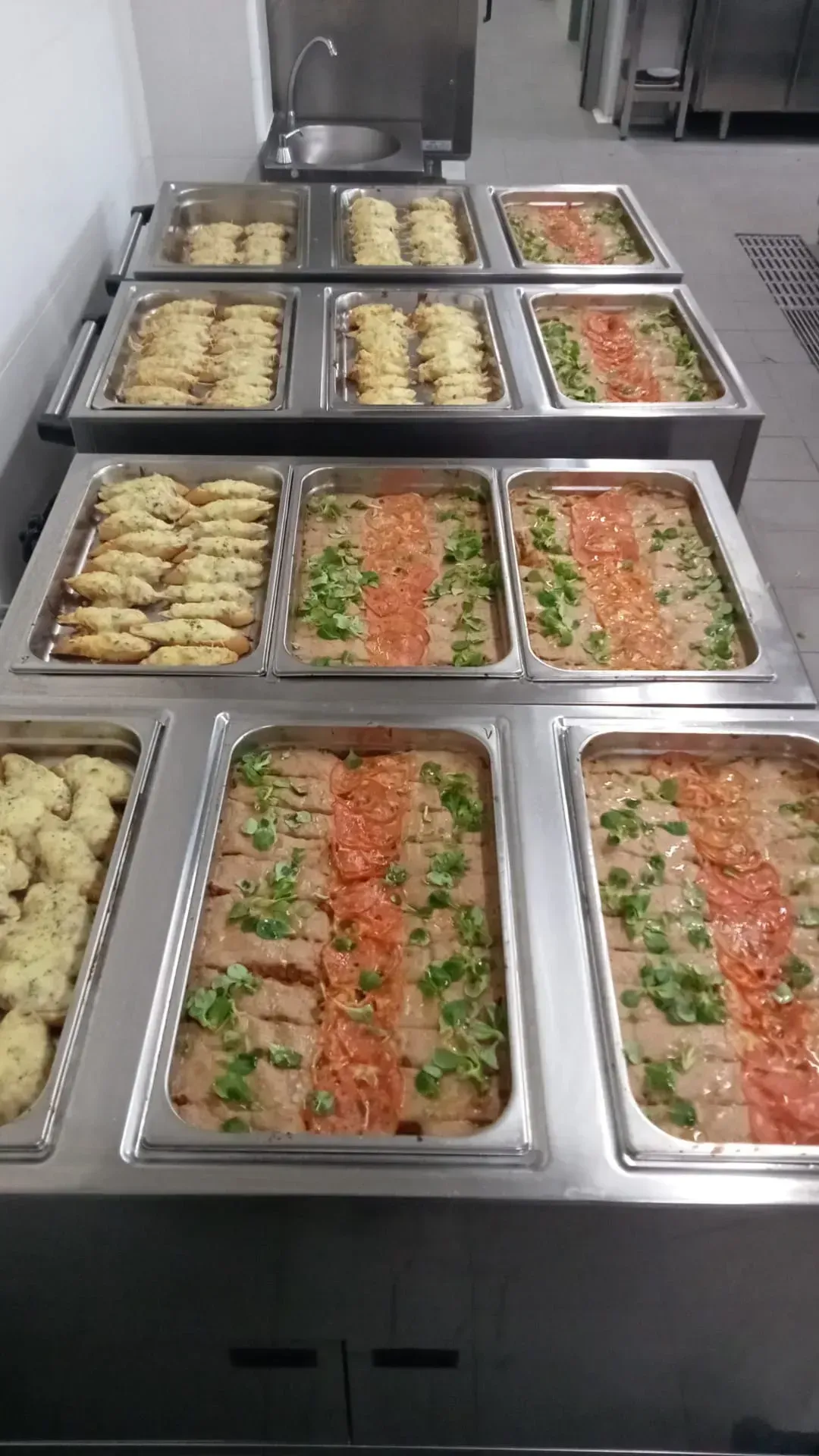 Una fila de bandejas de acero inoxidable llenas de comida en una cocina.