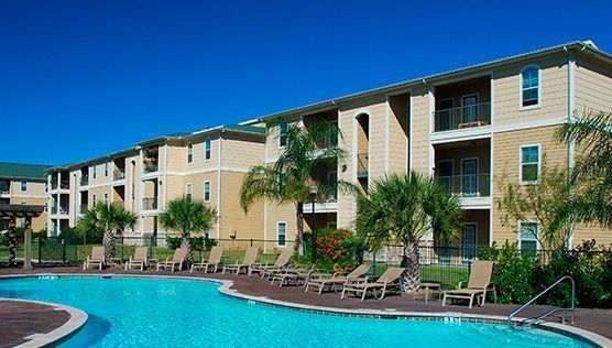 Edificio de apartamentos con piscina, palmeras y cielo azul claro.