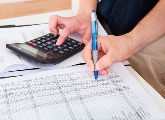 Persona que utiliza una calculadora y un bolígrafo para rellenar una hoja de cálculo.