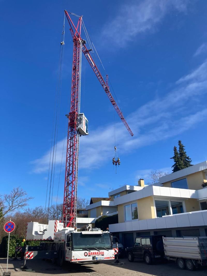 Ein roter Kran hebt unter blauem Himmel etwas in der Nähe von Gebäuden an.