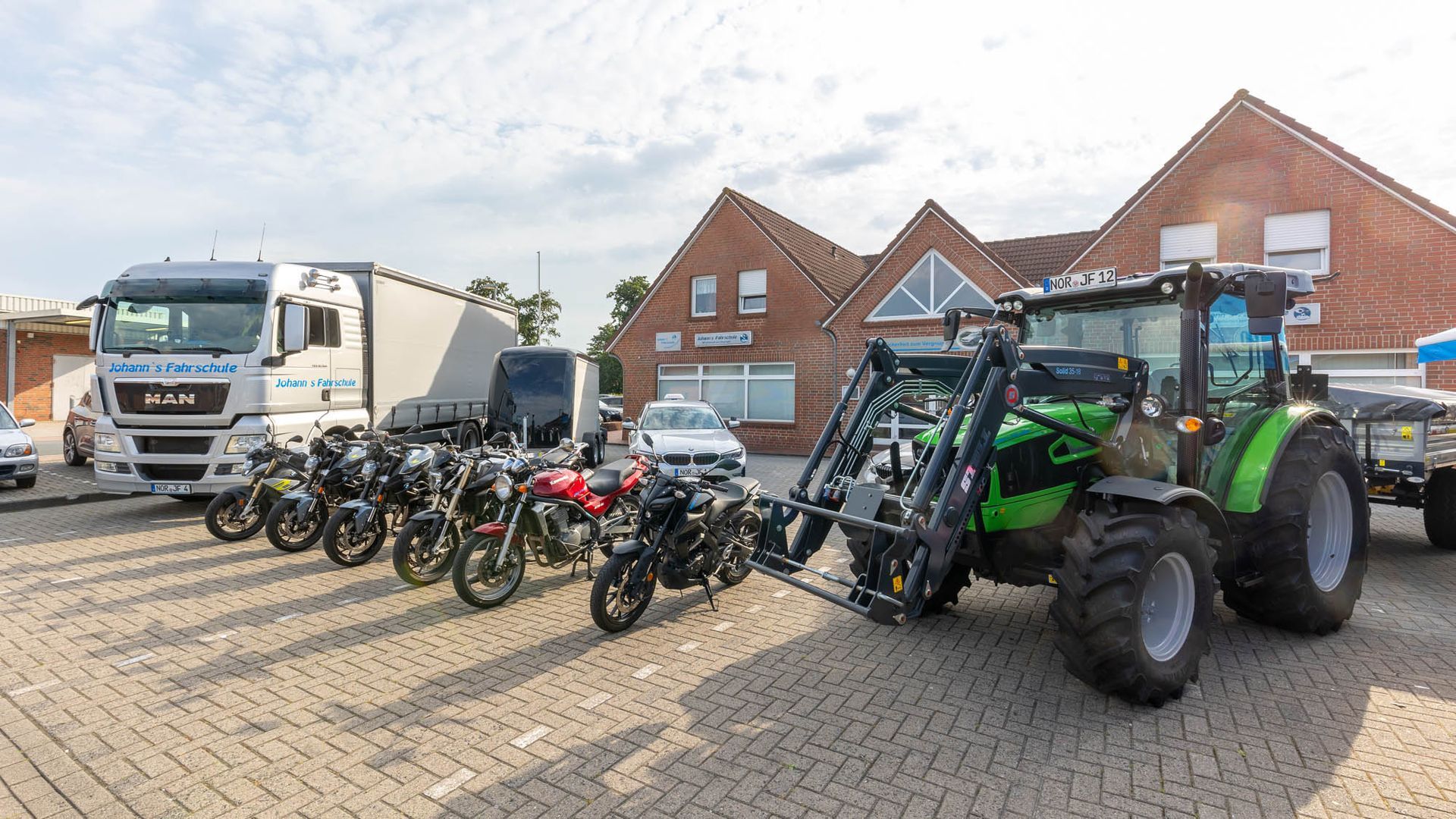 Auf einem Parkplatz neben einem Traktor steht eine Reihe Motorräder.