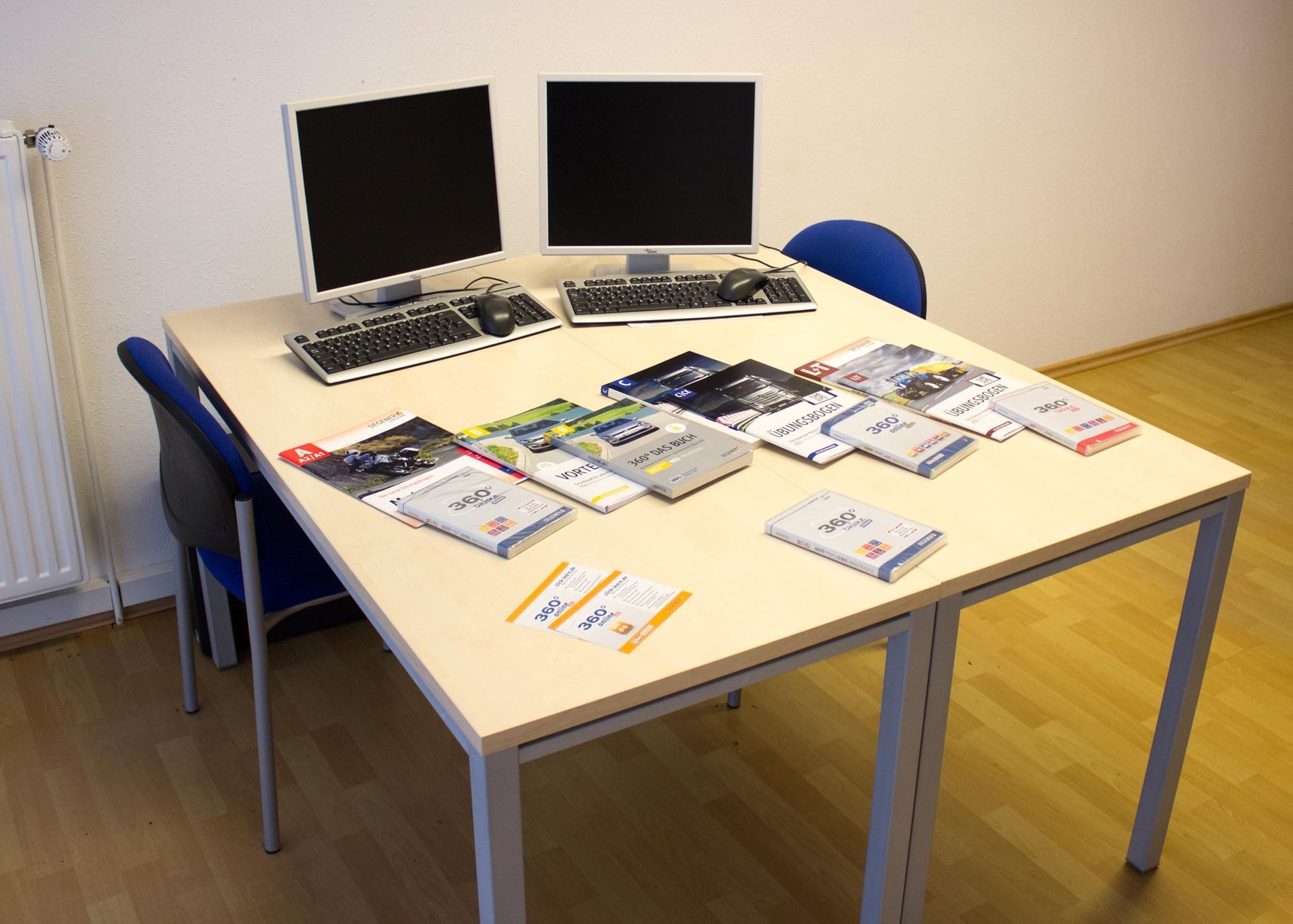 Ein Tisch mit zwei Computermonitoren und Büchern darauf