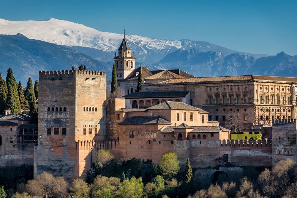 Un gran castillo situado en la cima de una colina con montañas al fondo.