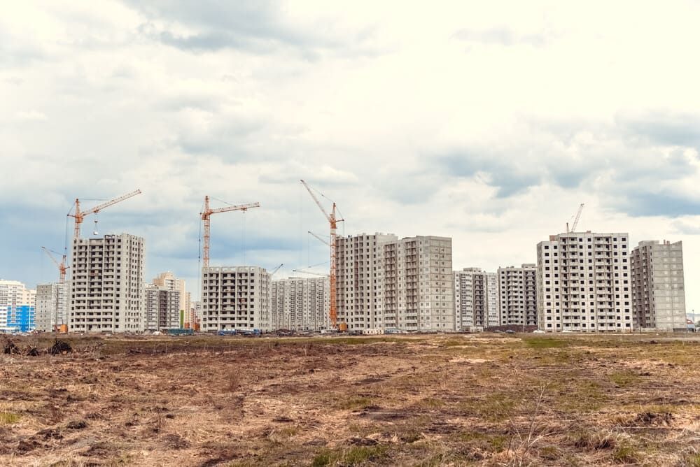 Una ciudad en construcción con grúas en primer plano y un campo al fondo.
