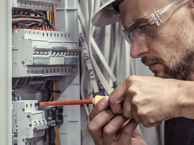 Un hombre está trabajando en una caja eléctrica con un destornillador.