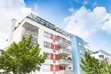 Ein großes Mehrfamilienhaus mit vielen Balkonen und Bäumen davor.