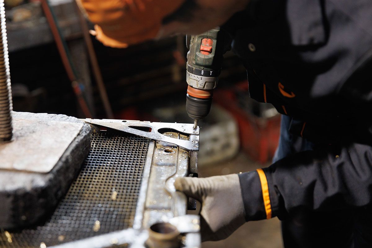 Homme qui perce un radiateur automobile à l'aide d'une visseuse