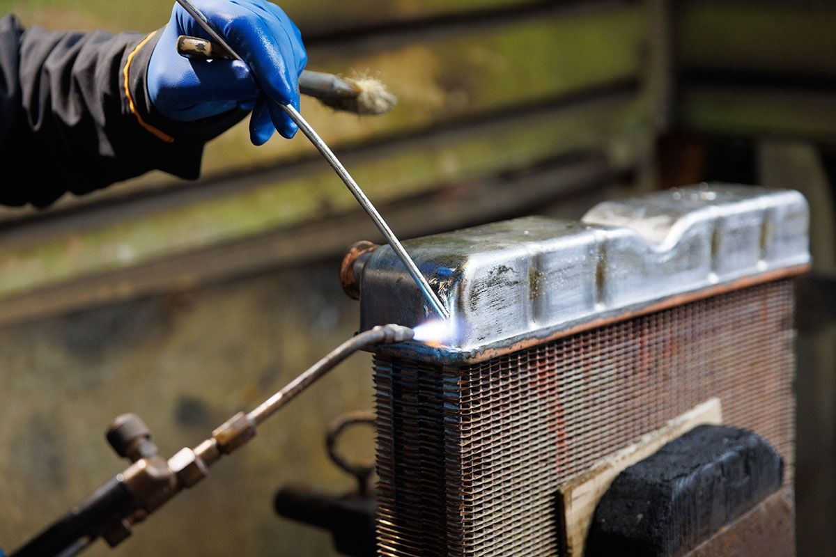 Homme qui soude avec une baguette de brasure un radiateur automobile
