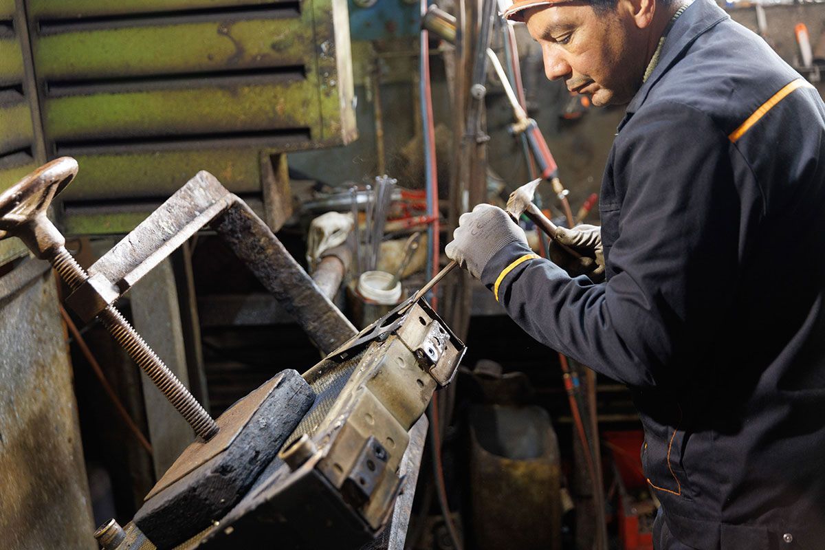 Homme qui utilise un marteau pour façonner un radiateur automobile