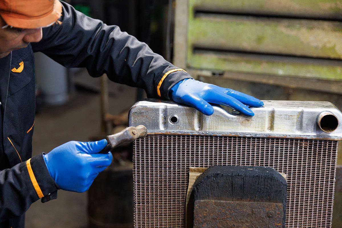 Ouvrier qui soude le radiateur d'une vieille voiture