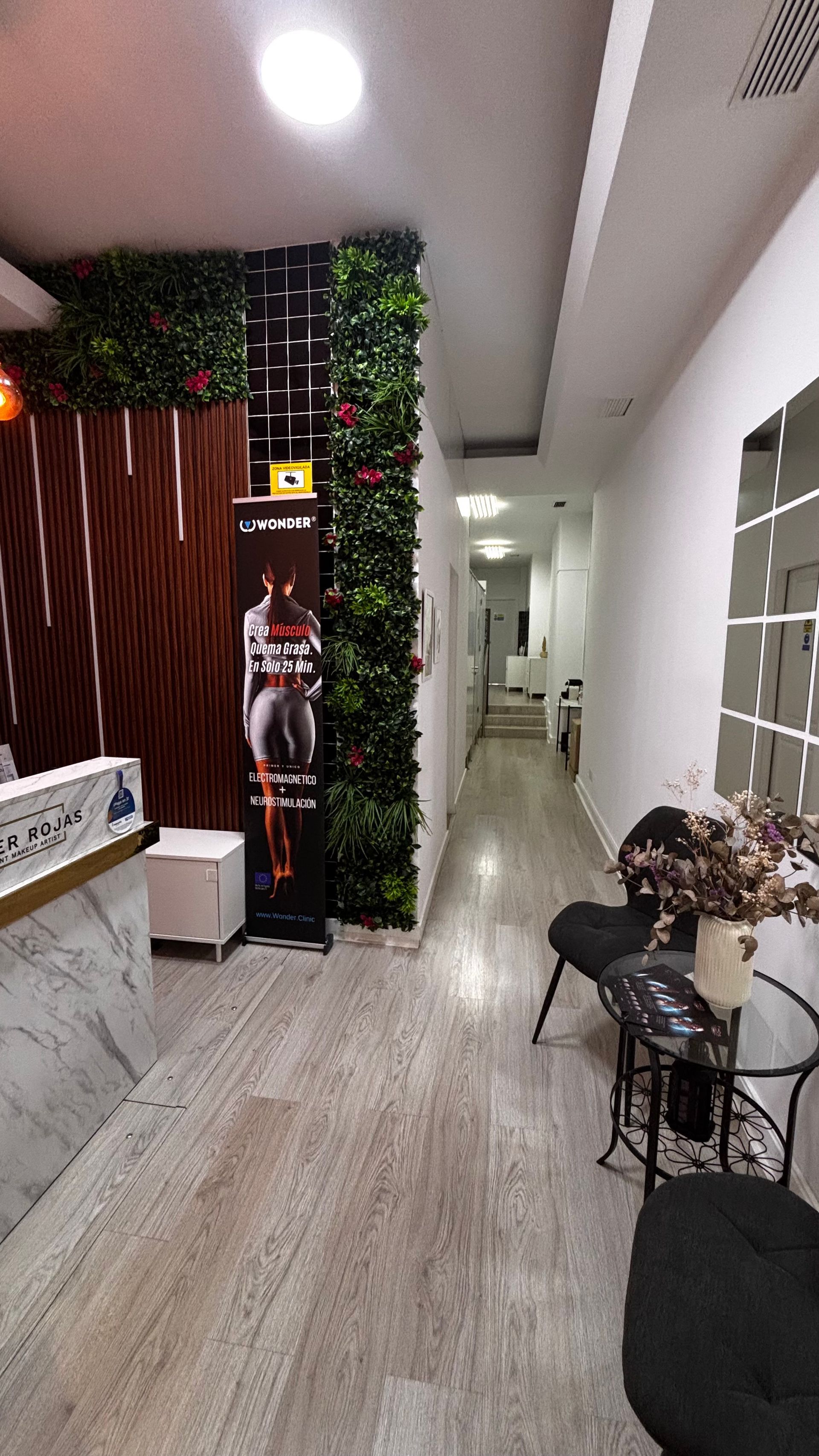 Lobby con jardín vertical, muro de madera, zona de espera con sillas y pasillo.