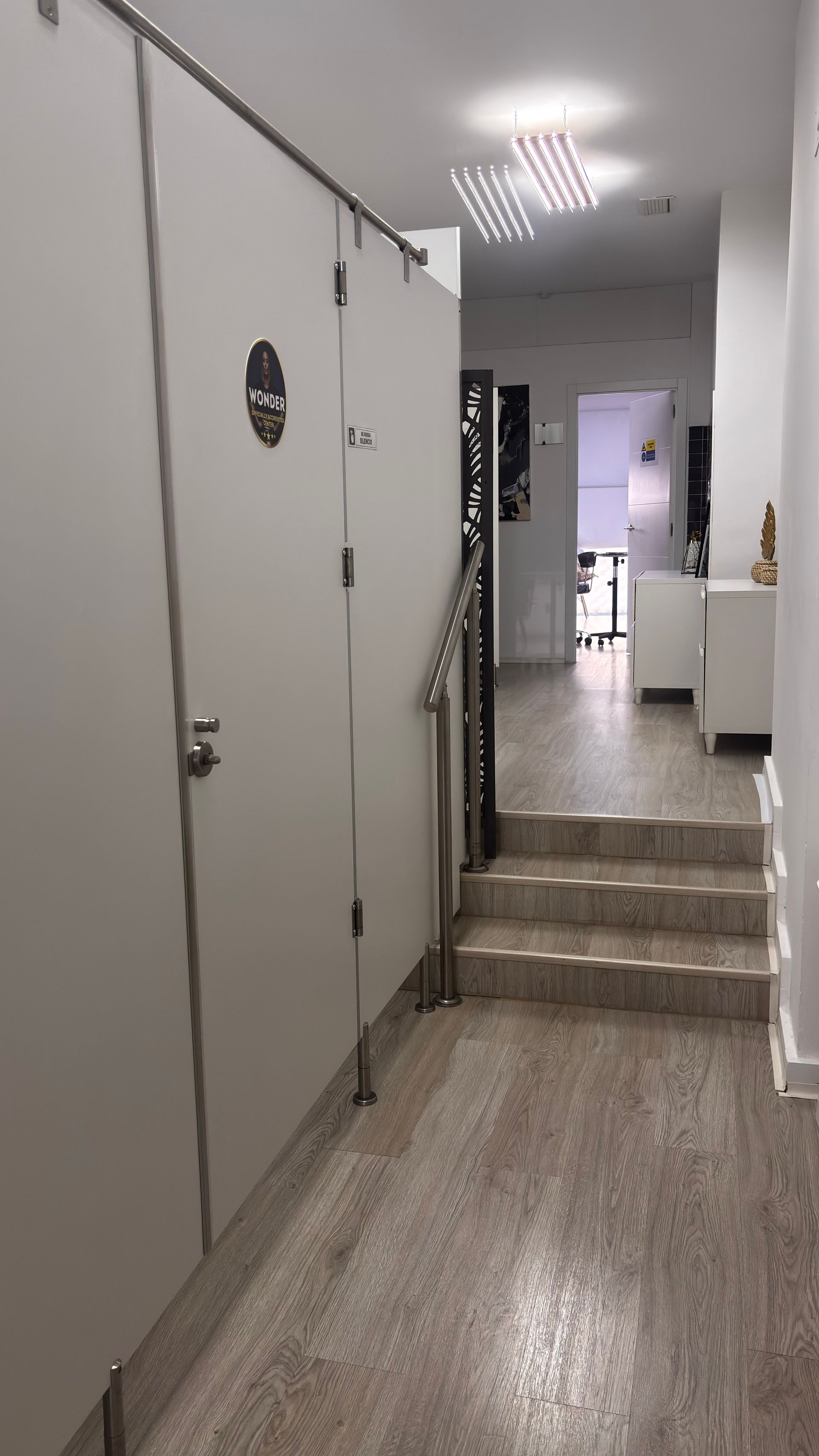 Las puertas blancas de los cubículos bordean un pasillo con escalones. Se ve una lámpara.