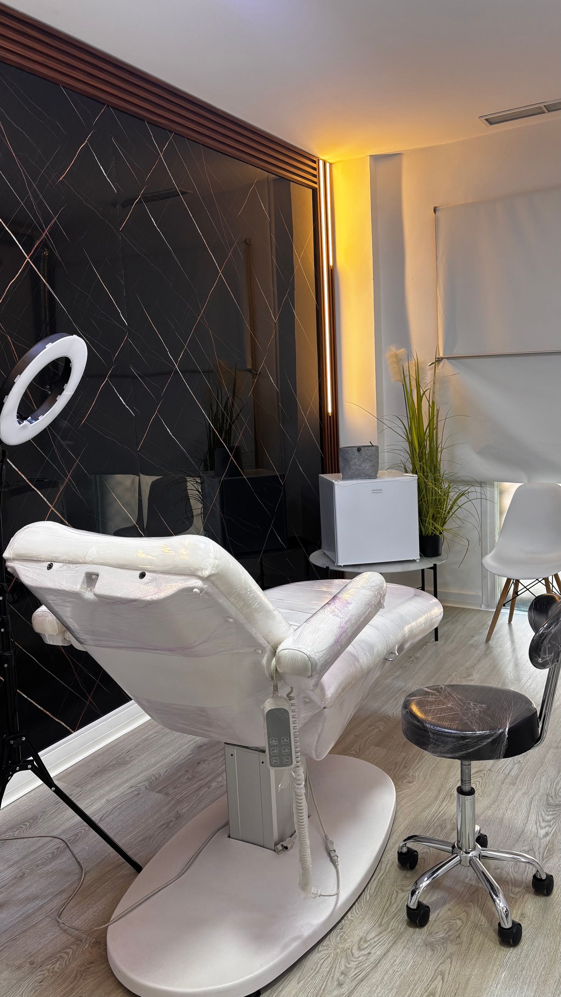 Sala de tratamientos de salón con silla blanca, pared negra e iluminación.