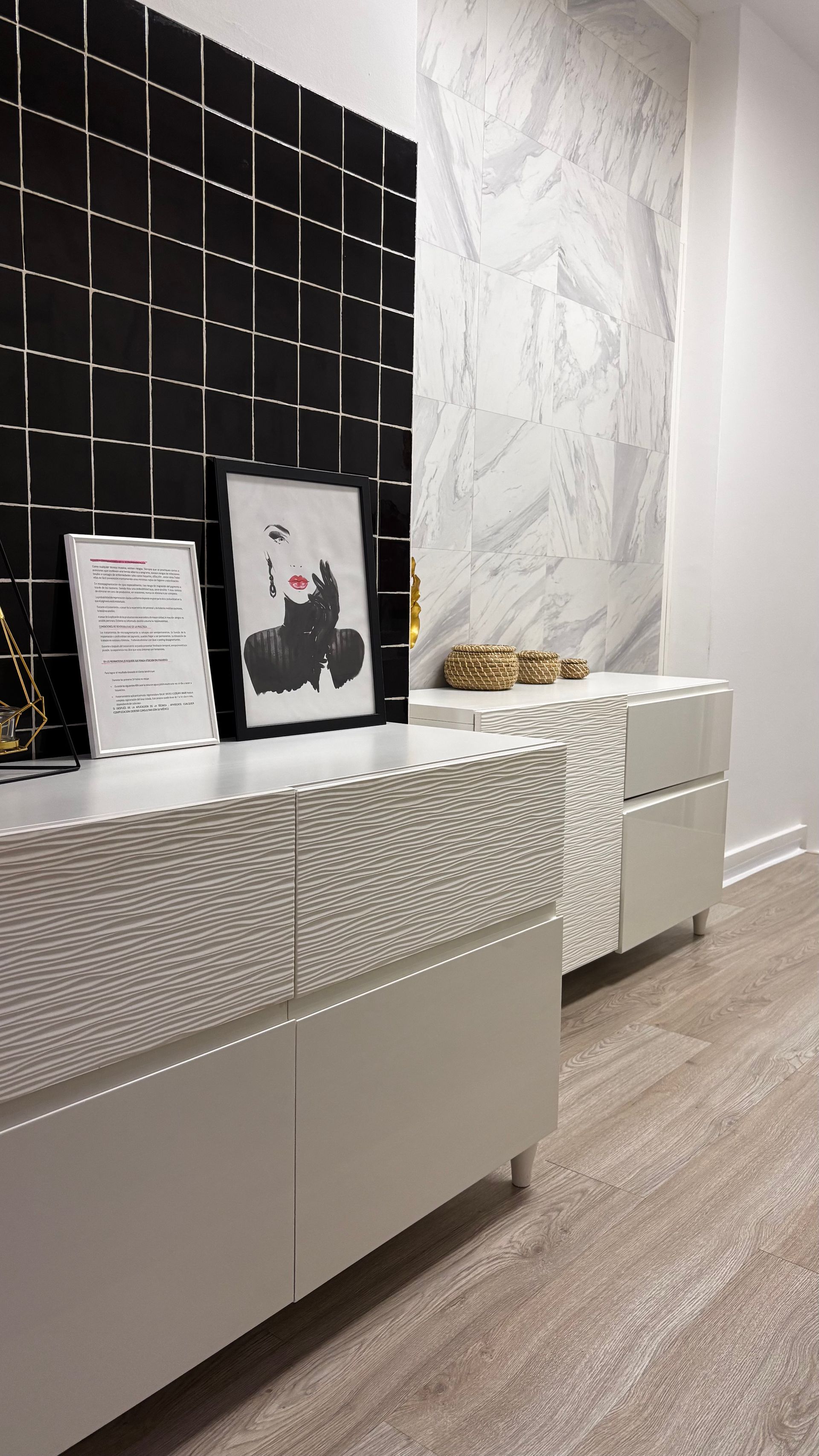 Consola moderna con fachada blanca texturizada, arte, contra pared de azulejos negros y mármol.