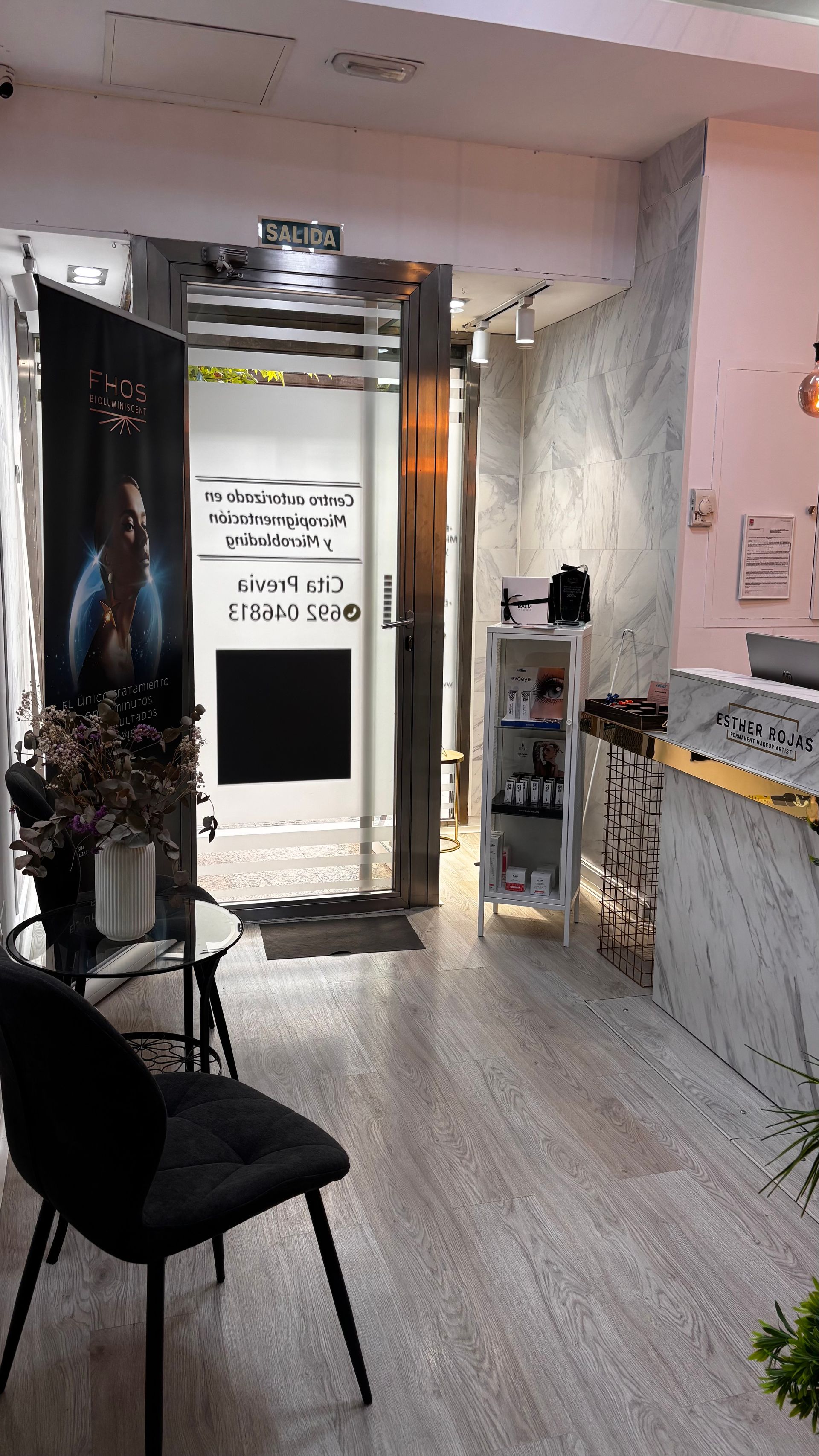 Interior de una tienda con mostrador de mármol, zona de espera con silla y puerta abierta.