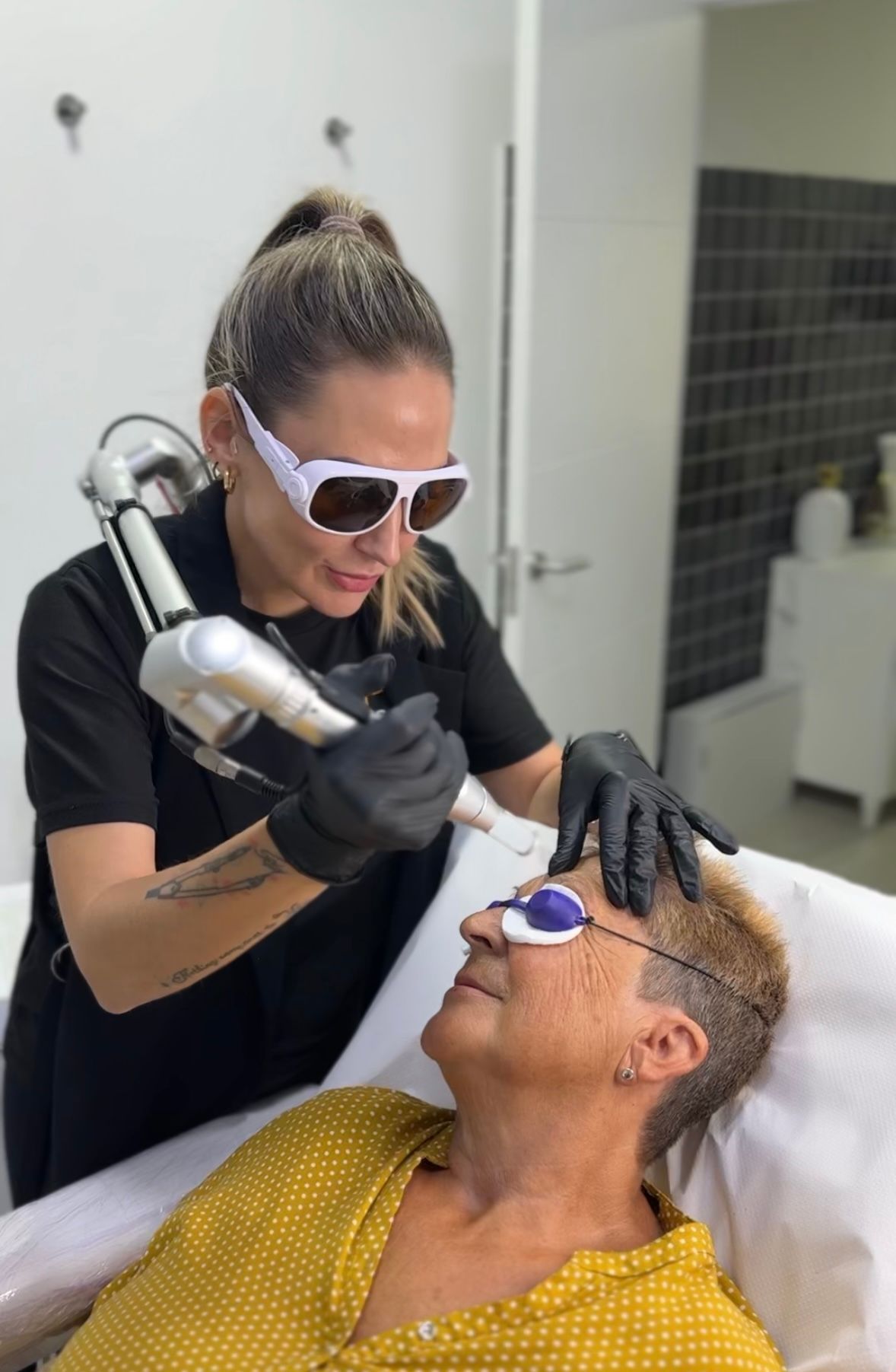 Una mujer que lleva una mascarilla y guantes se está haciendo un tatuaje en el ojo.
