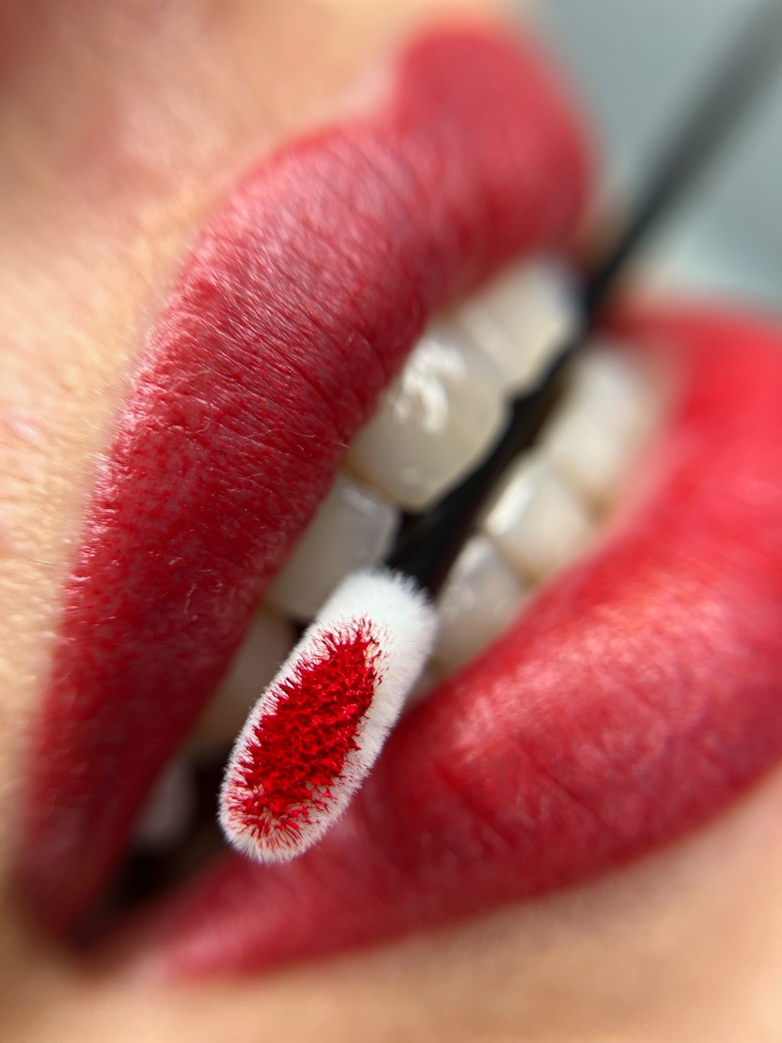 Primer plano de unos labios rojos sosteniendo un aplicador de lápiz labial, con pigmento rojo en el aplicador.