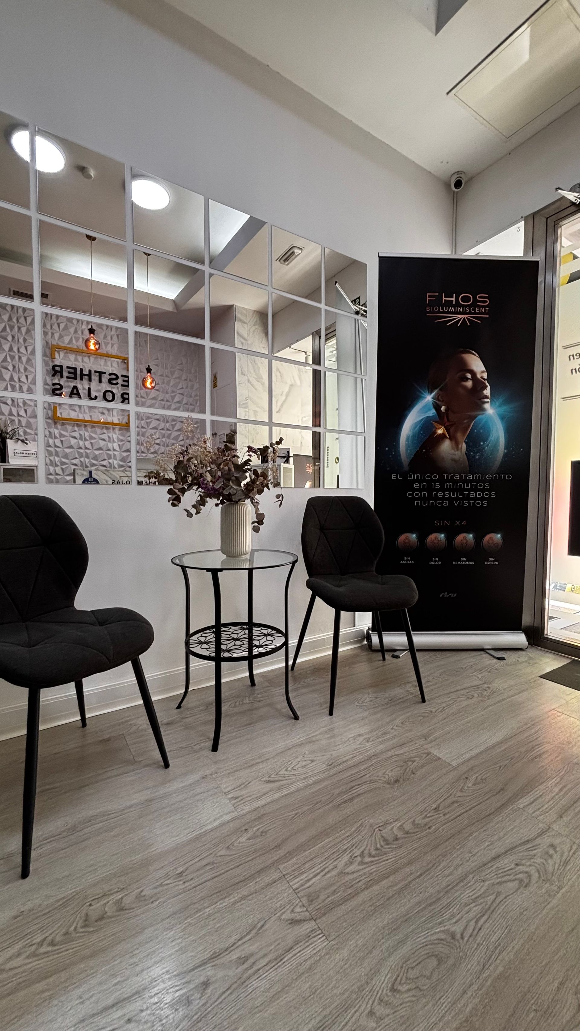 Una zona de espera en un salón con sillas, una mesa, un póster y una pared de espejos.