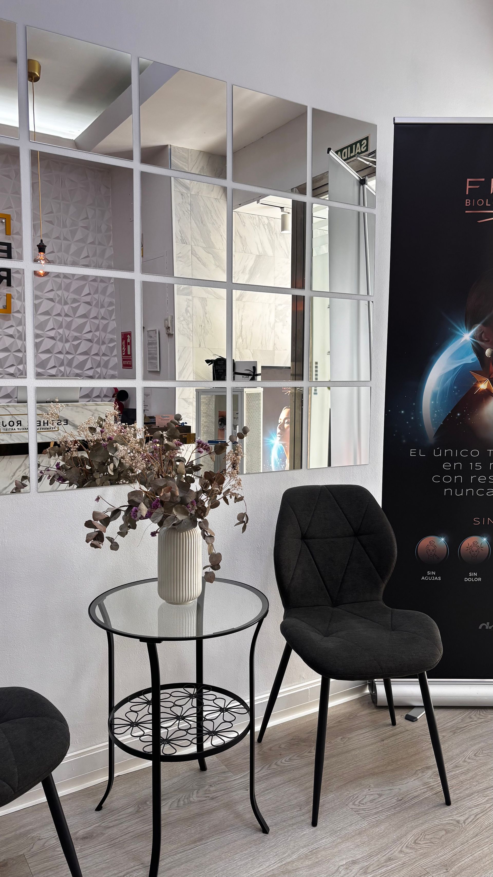 Una habitación con un espejo decorativo, una mesa pequeña, una silla negra y un póster.