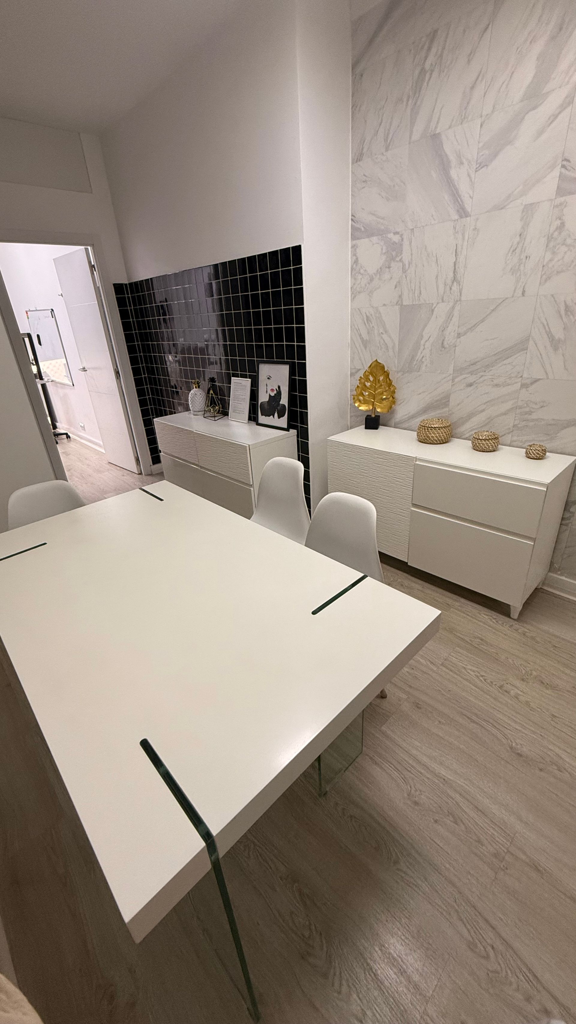 Comedor minimalista blanco con mesa y dos armarios blancos. Pared con estampado de mármol.
