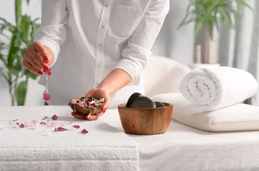 Una mujer sostiene un recipiente con flores y piedras sobre una mesa en un spa.