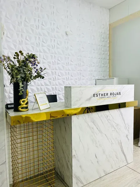 Un mostrador de recepción blanco y dorado con un jarrón de flores encima.