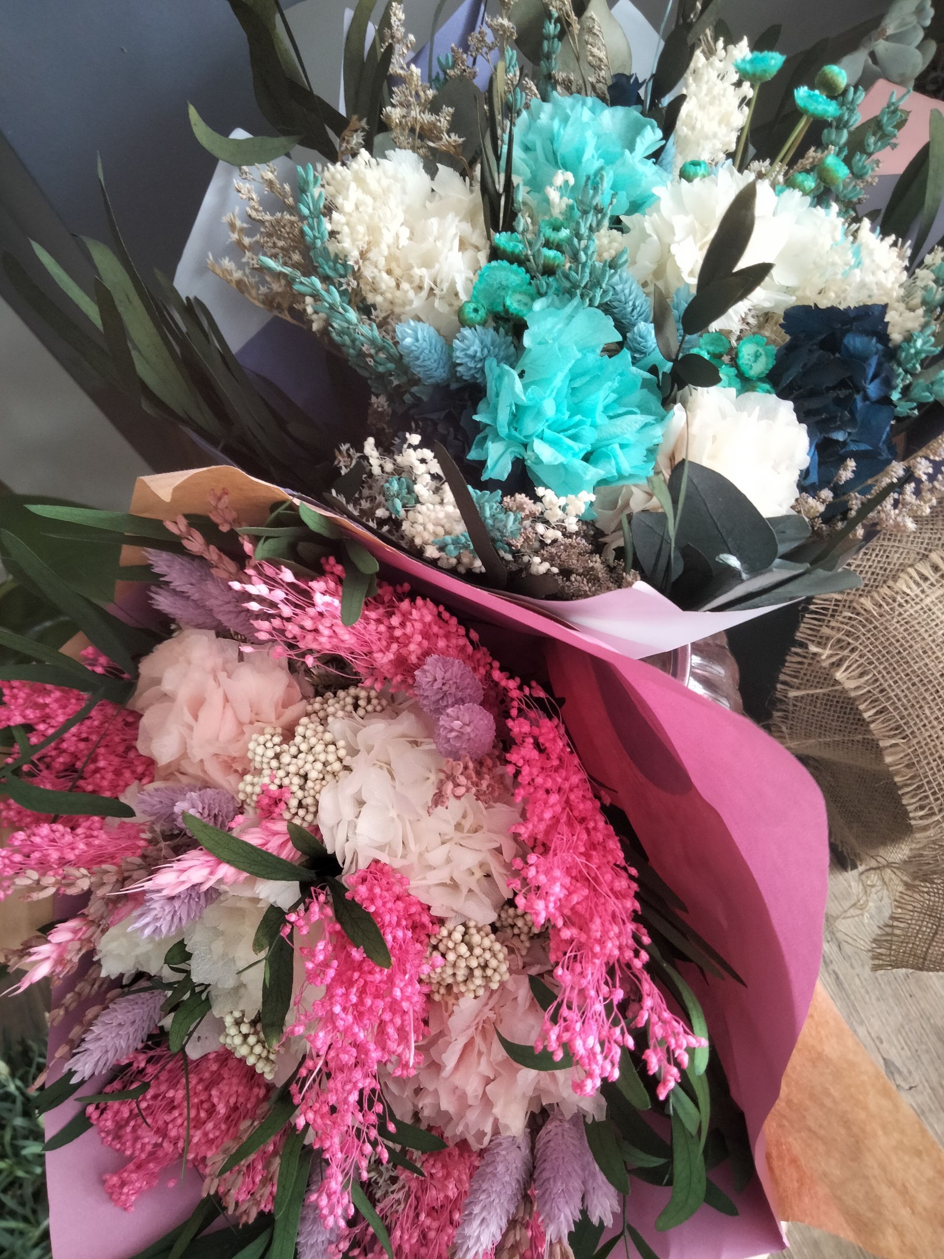 Deux bouquets de fleurs séchées ; l'un dans les tons de bleu et de blanc, l'autre dans les tons de rose, emballés dans du papier.