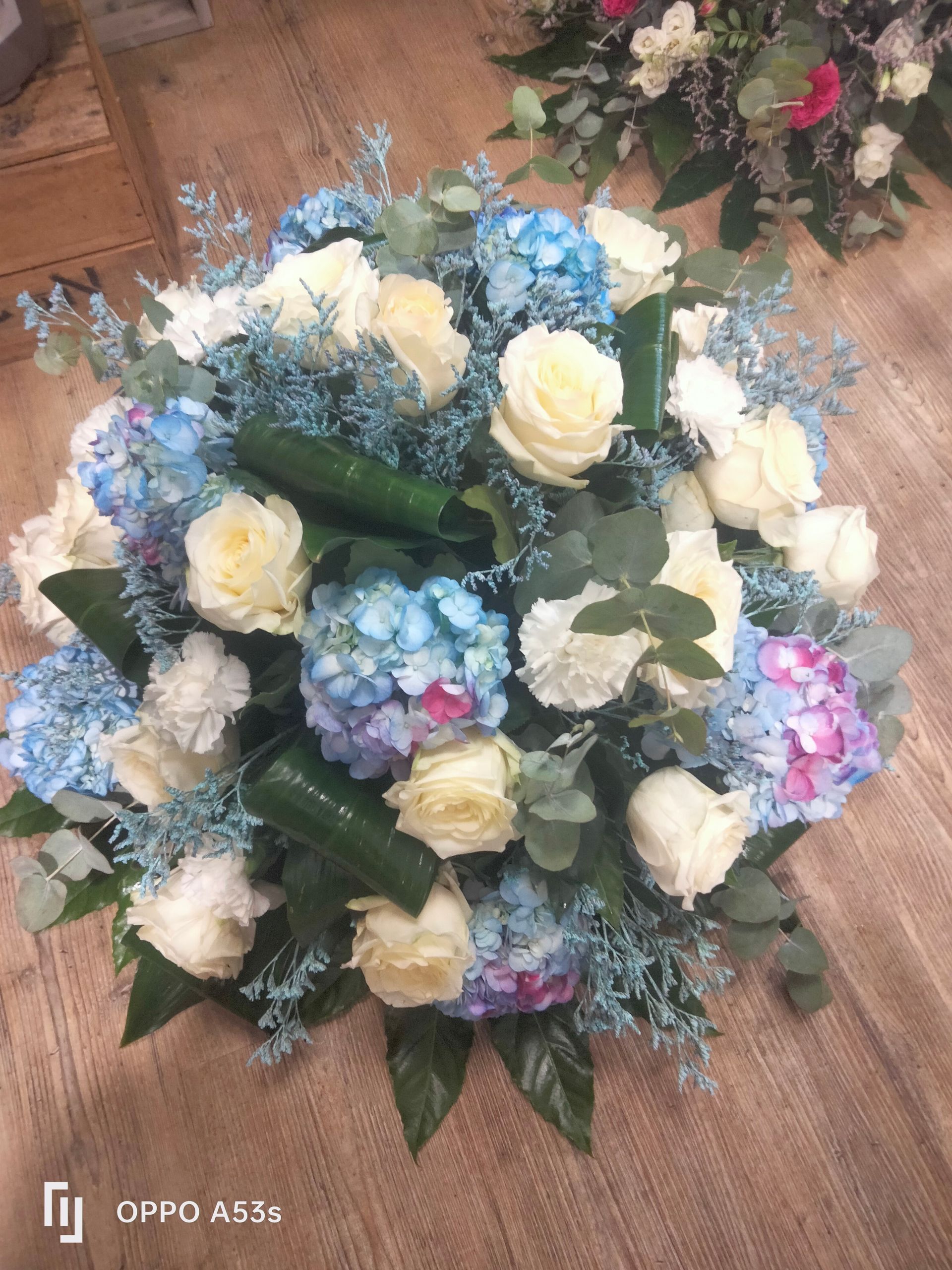 Un somptueux bouquet de roses blanches, d'hortensias bleus et de feuillage vert repose sur un plancher en bois.