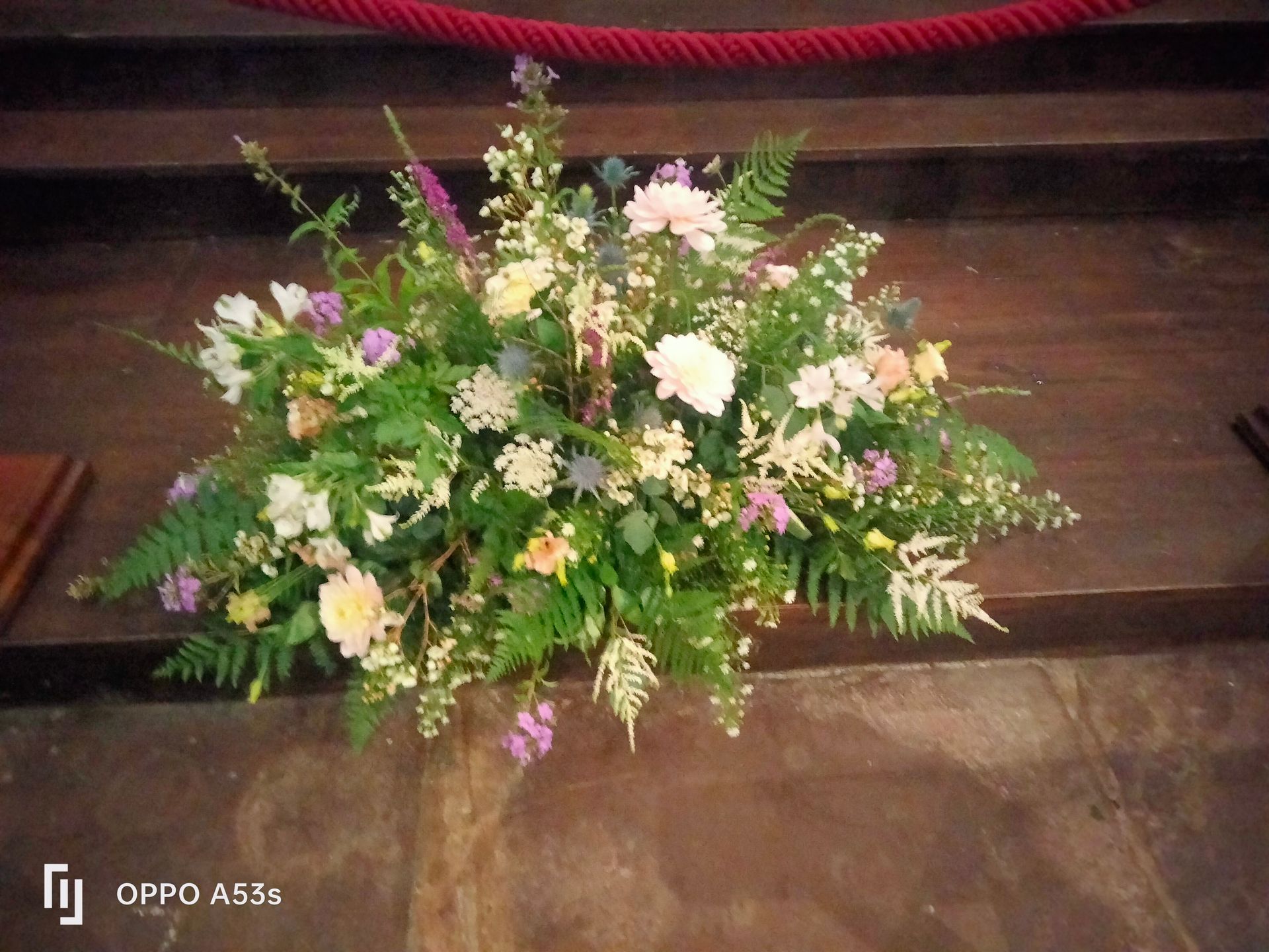 Une somptueuse composition florale, mêlant fleurs blanches, roses et violettes et feuillage vert, orne des marches en bois.