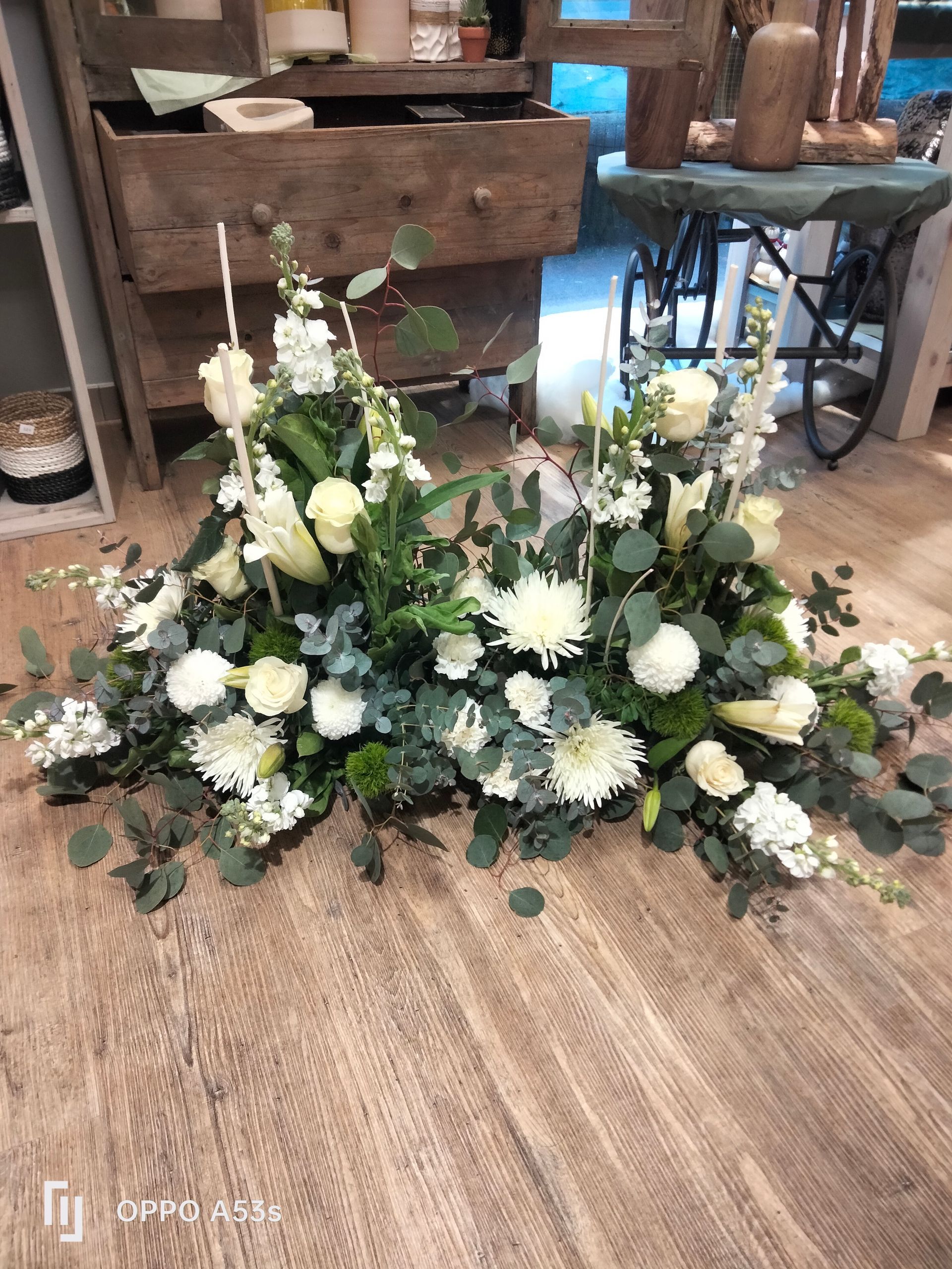 Une grande et luxuriante composition florale de fleurs blanches et de feuilles d'eucalyptus vertes repose sur un parquet clair.