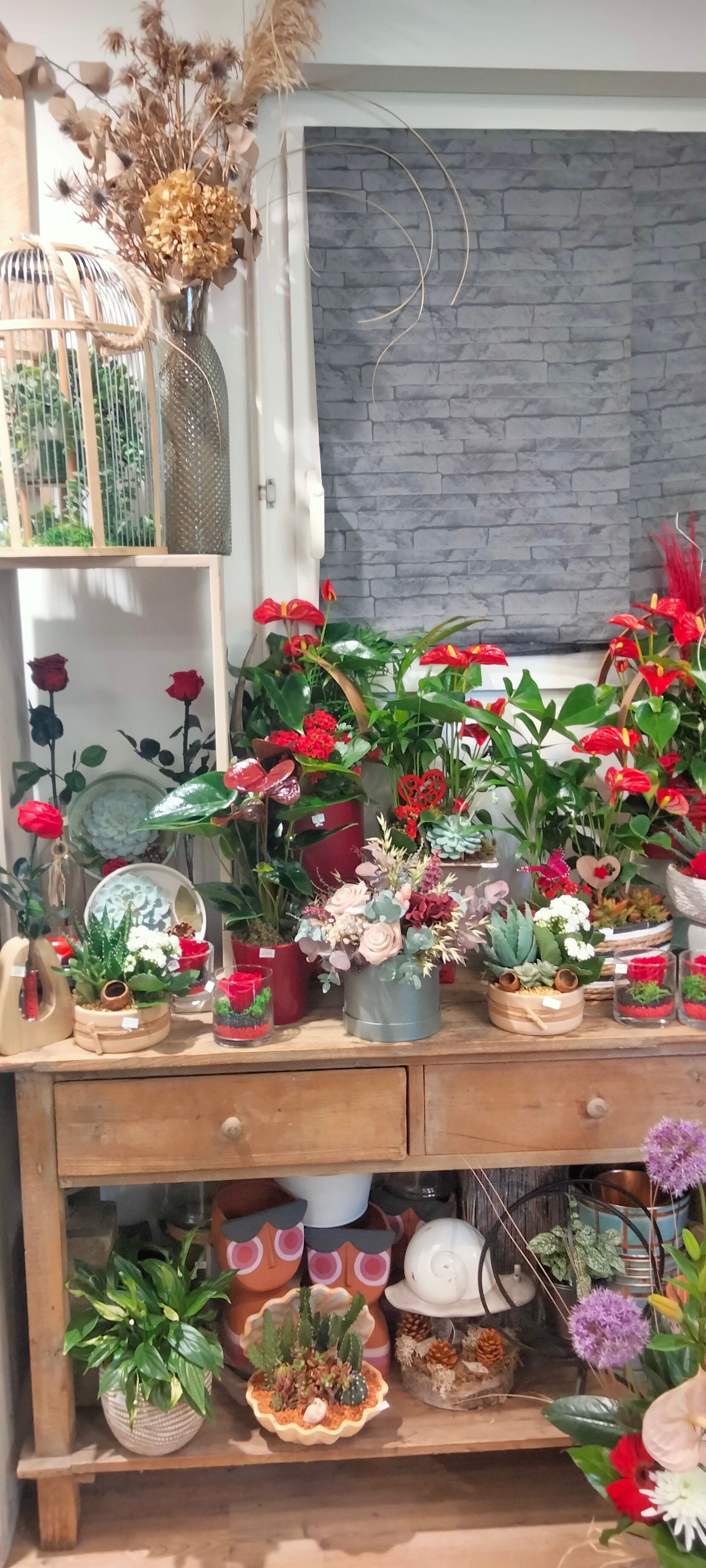 Une table en bois présentant diverses plantes en pot, des fleurs et des objets décoratifs dans un magasin.