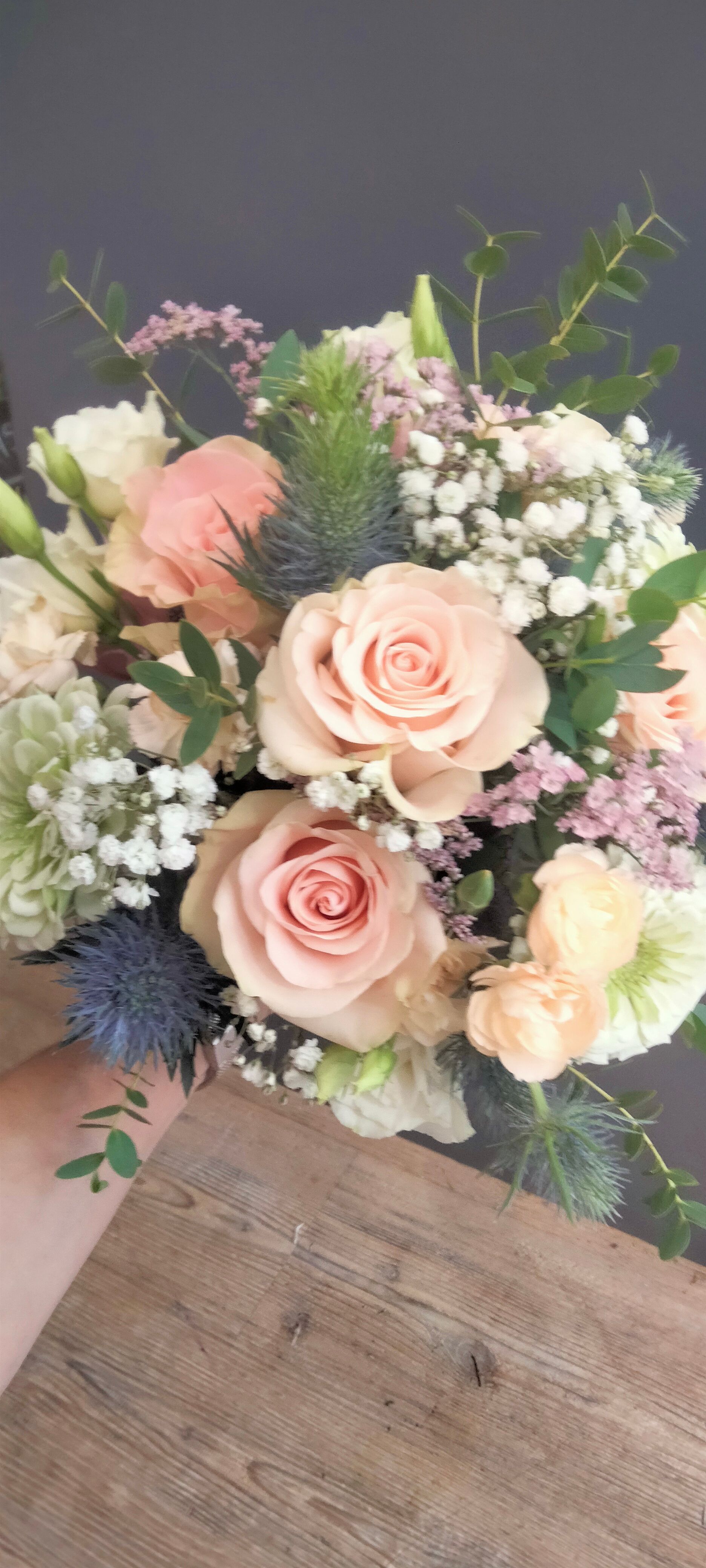 Deux personnes disposent un bouquet de fleurs composé de tulipes jaunes, d'hortensias roses et de verdure sur une table en bois.