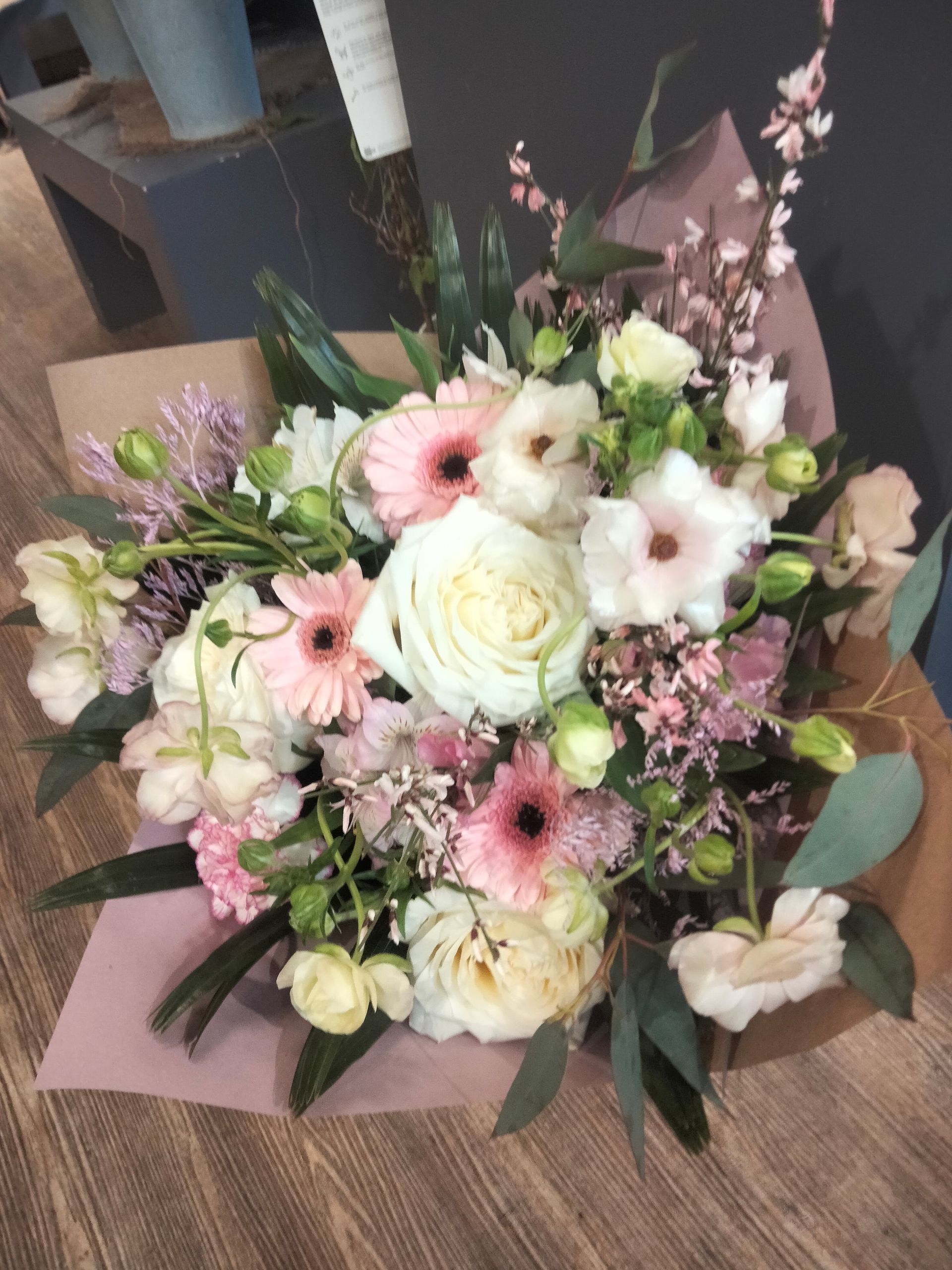 Un bouquet romantique de fleurs rose pâle et blanches, comprenant des roses et des gerberas, enveloppé dans du papier kraft doux.