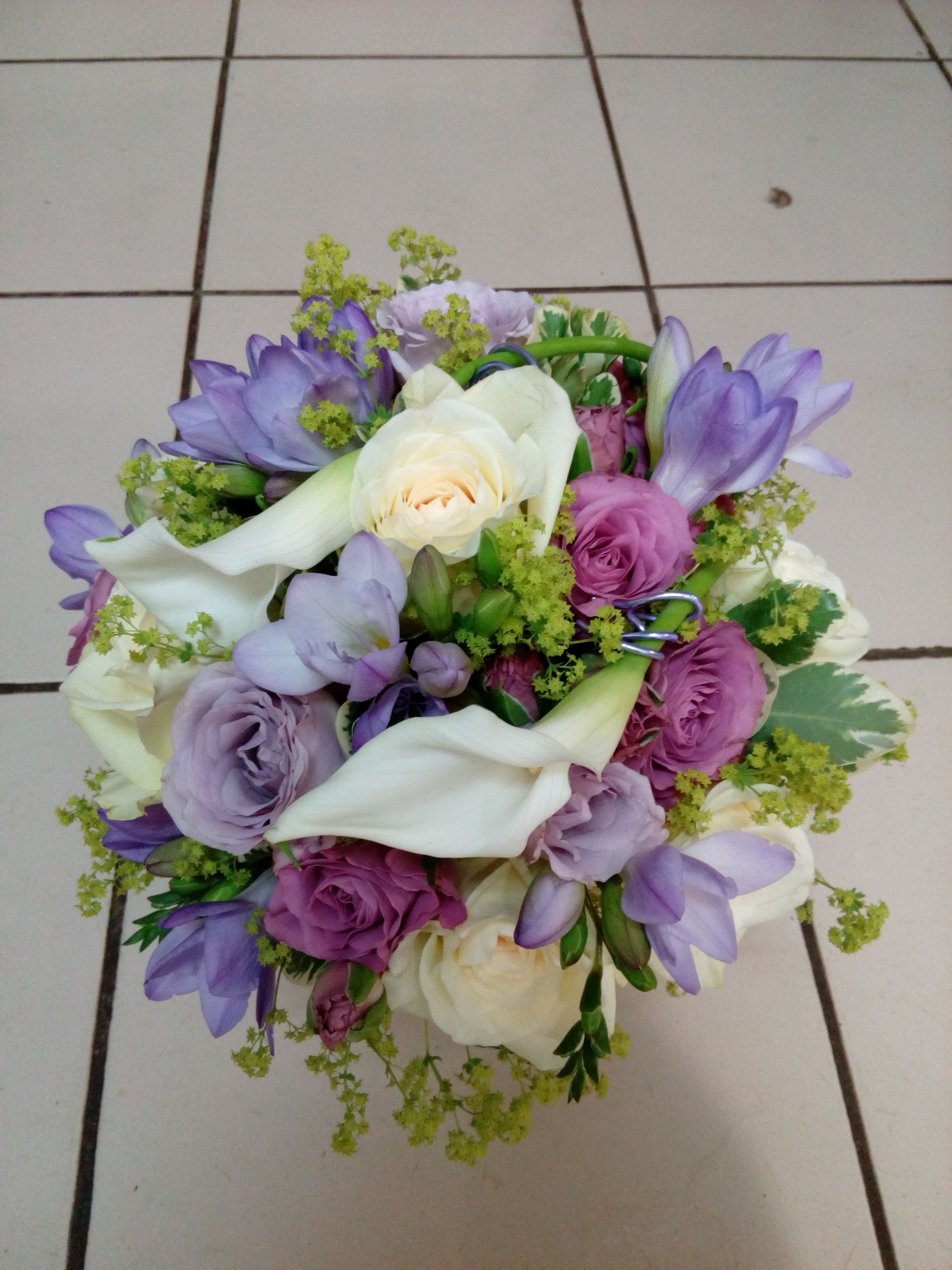 Un bouquet de callas blanches, de roses violettes claires et foncées, de freesias violets et de petites fleurs vertes d'accompagnement.