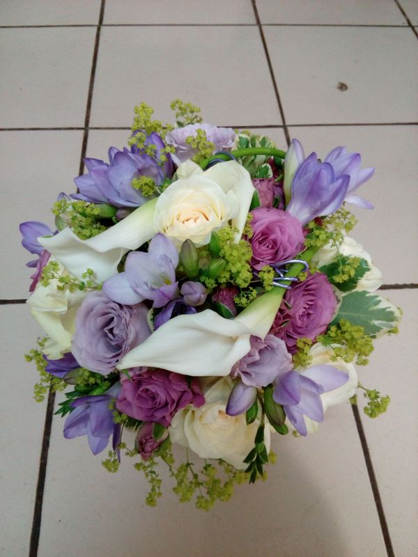Un bouquet de callas blanches, de roses violettes claires et foncées, de freesias violets et de petites fleurs vertes d'accompagnement.