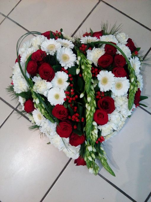 Une composition florale en forme de cœur avec des roses rouges, des gerberas blancs et des tiges vertes sur un sol carrelé.