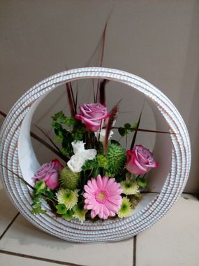 Un arrangement floral de roses roses, de fleurs blanches et de touches de vert, à l'intérieur d'un cadre blanc circulaire texturé.