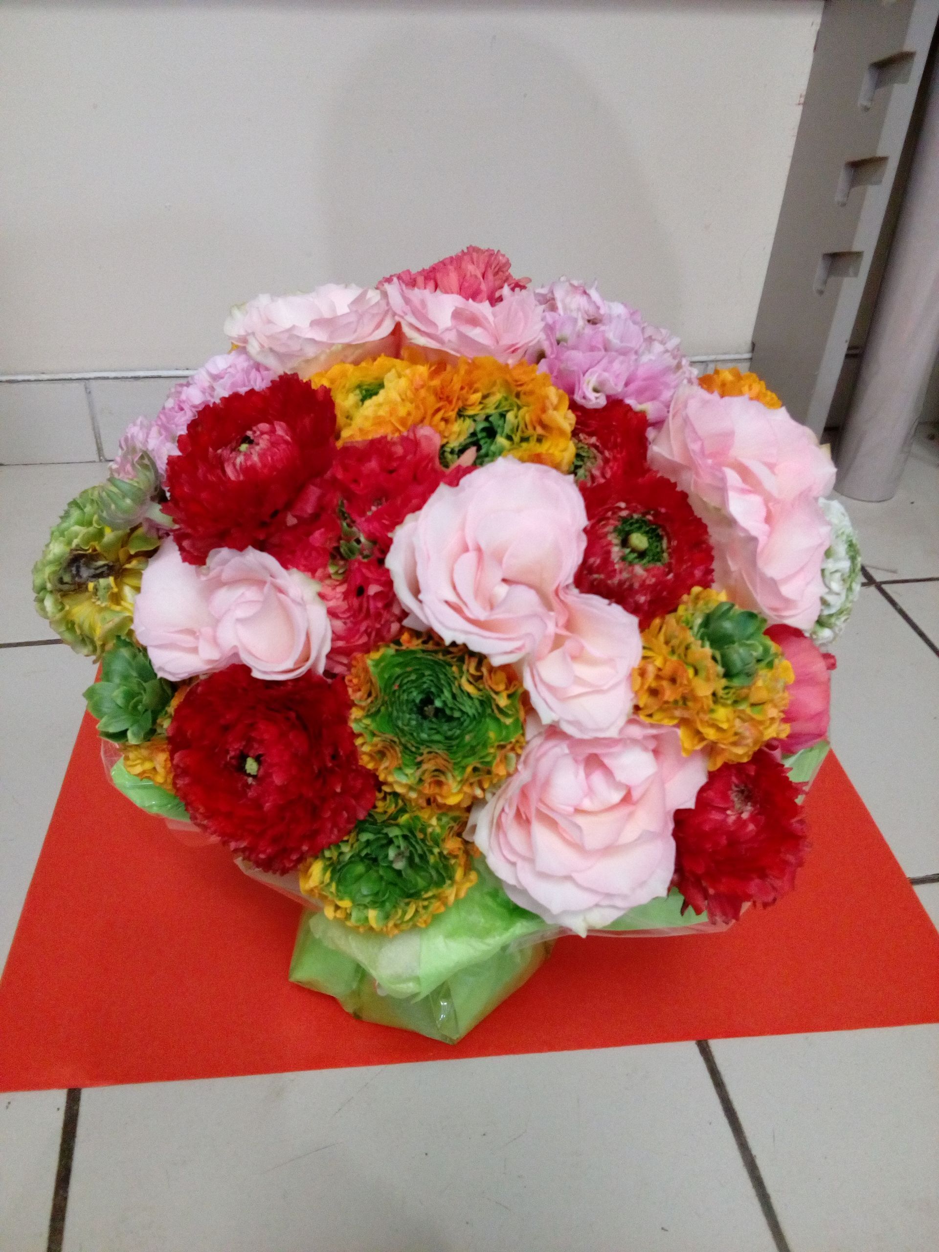 Un bouquet éclatant et multicolore composé de renoncules roses, rouges, oranges et vertes sur un tapis rouge.