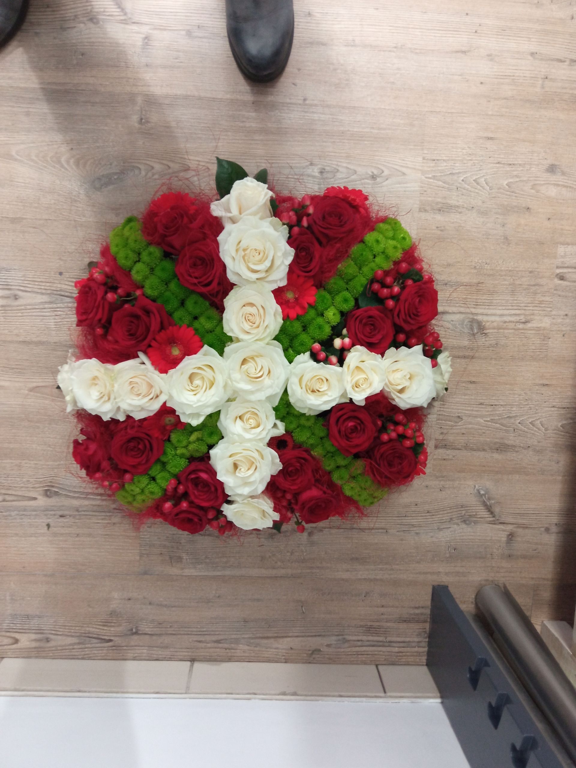 Un arrangement floral carré composé de roses blanches formant une croix, entourées de roses rouges et de fleurs vertes.