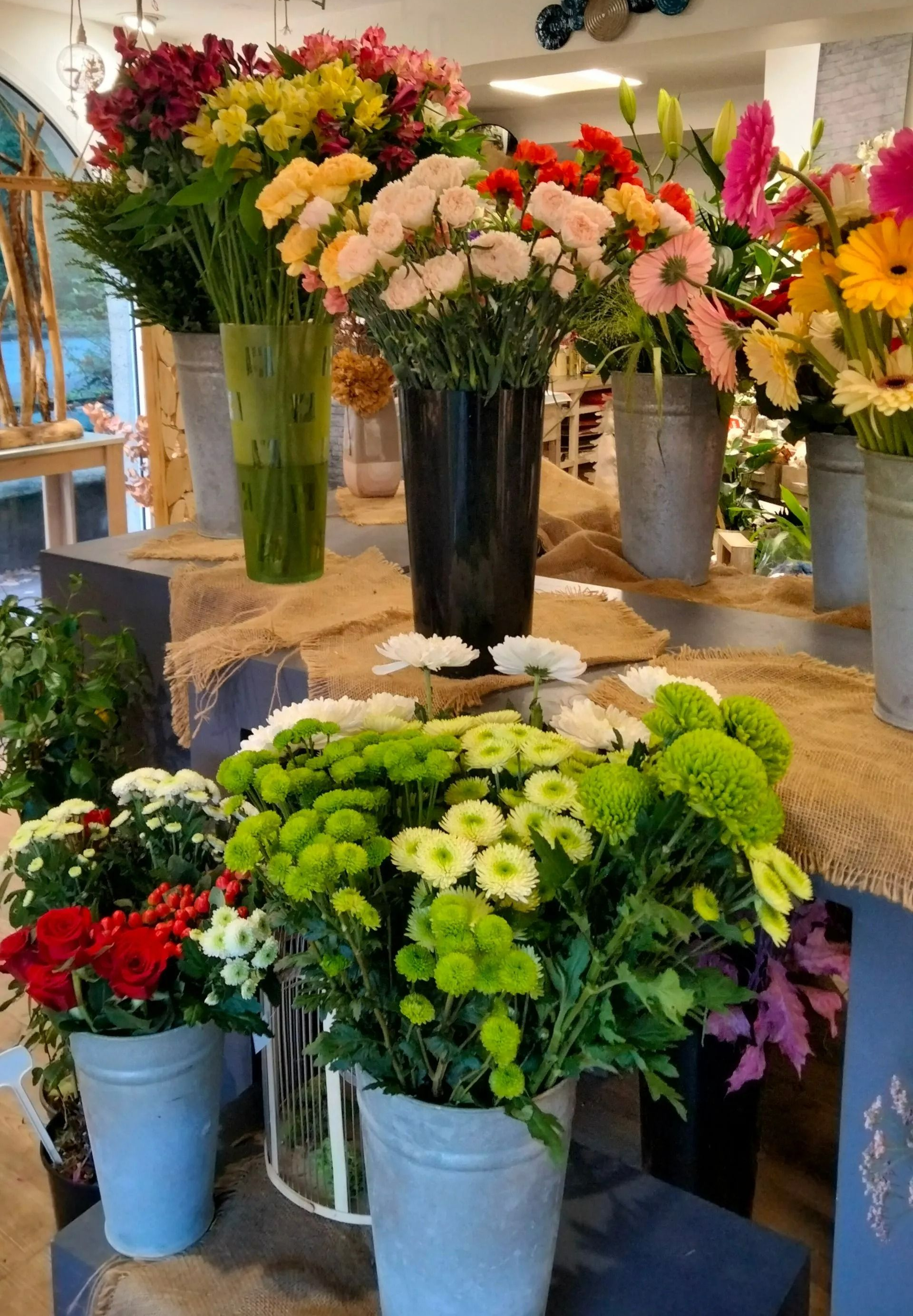 Dans une boutique de fleurs, une variété de bouquets de fleurs colorés sont disposés dans des vases et des seaux en métal sur des étagères.
