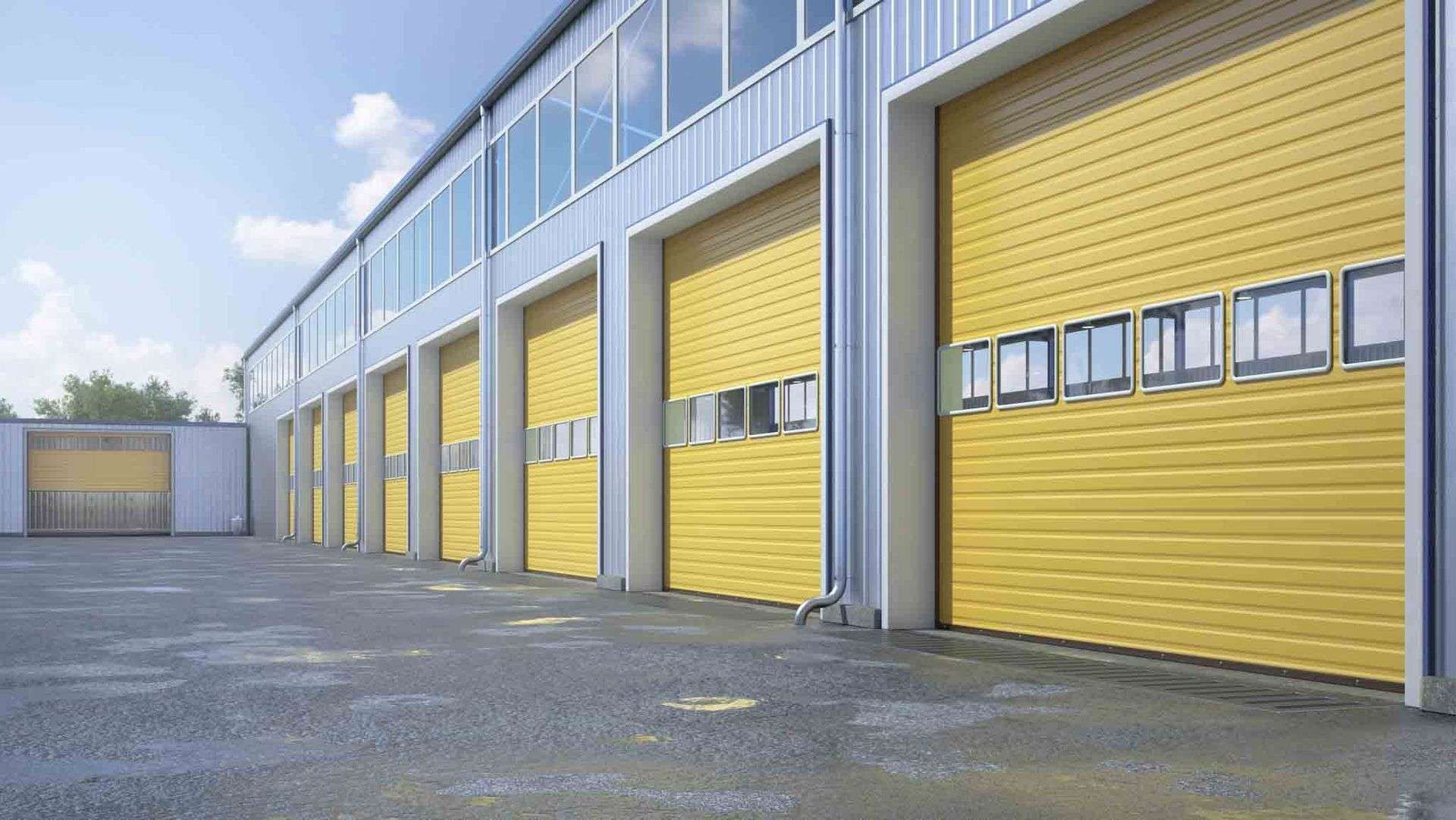 Un edificio industrial amarillo con múltiples puertas enrollables. La luz entra por las pequeñas ventanas sobre las puertas.