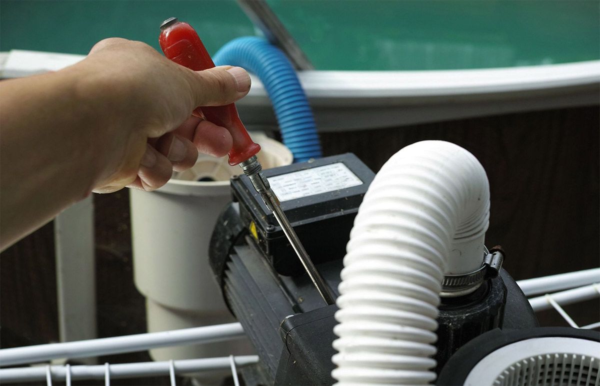 Una persona está arreglando una bomba de piscina con un destornillador.