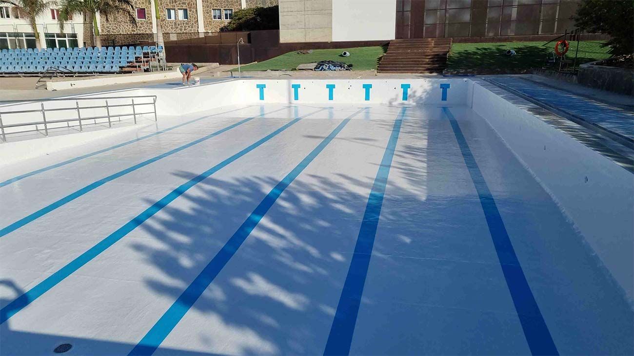 Una piscina vacía con líneas azules y un edificio al fondo.