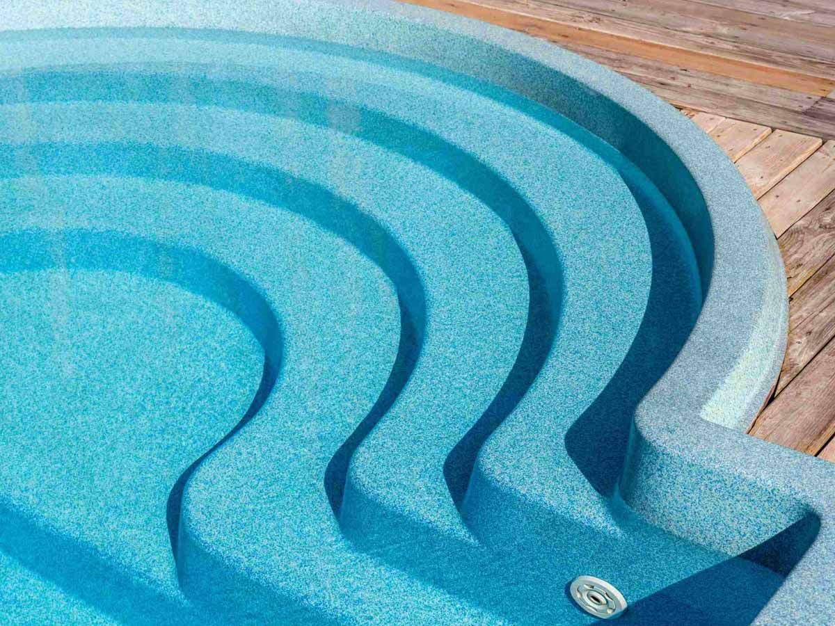 Una piscina con agua azul y escaleras sobre un deck de madera.