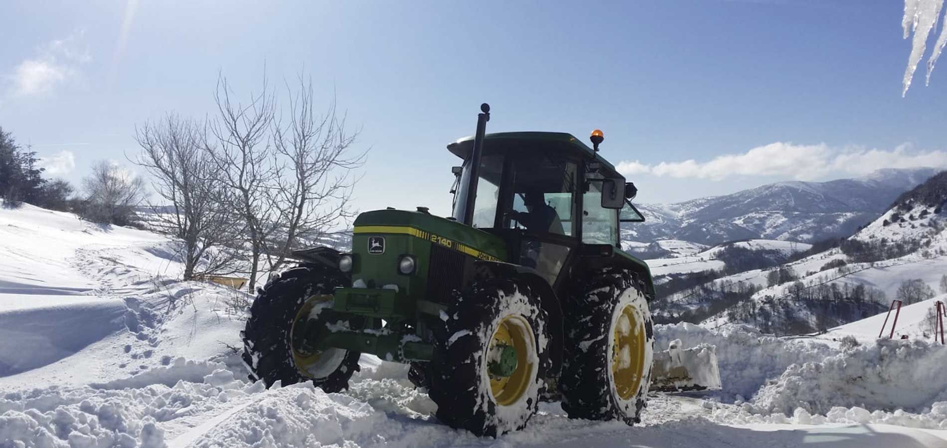 Un tractor verde circula por una carretera cubierta de nieve.