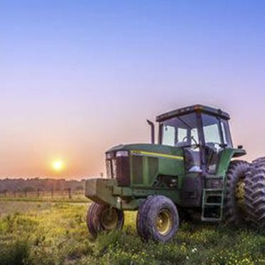 Un tractor verde está estacionado en un campo al atardecer.