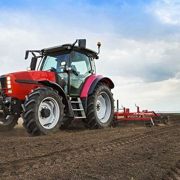 Un tractor rojo está arando un campo con un arado acoplado a él.