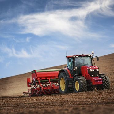 Un tractor rojo está arando un campo con una sembradora acoplada a él.