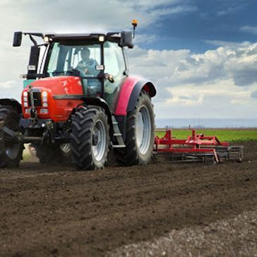 Un tractor rojo está arando un campo con un arado acoplado.